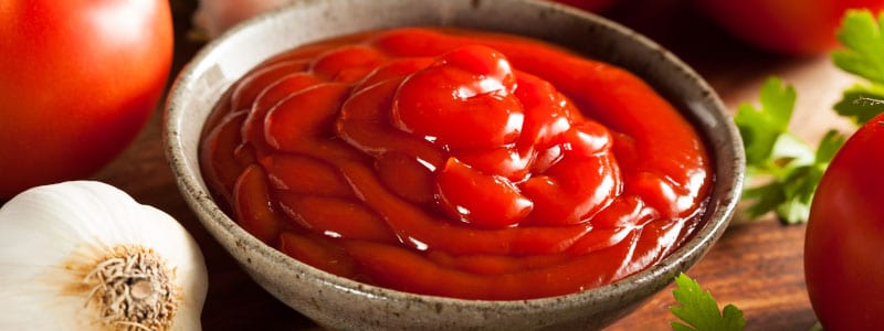 Ketchup in a wood bowl surrounded by tomatoes and garlic
