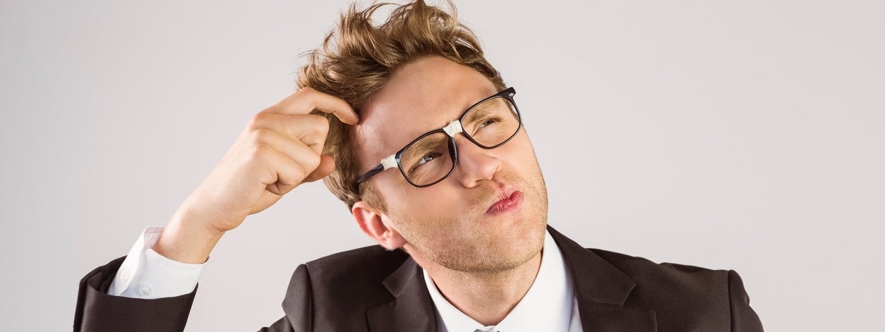 Young geeky businessman scratching his head on grey background