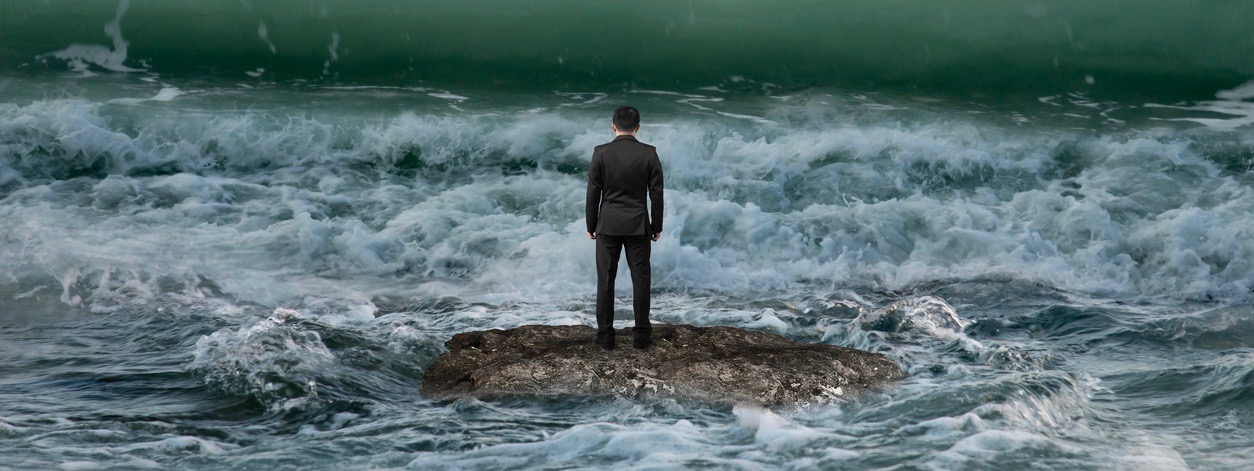 businessman standing on rock in the ocean facing oncoming waves