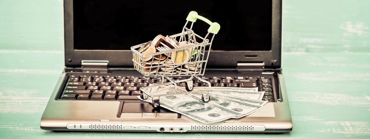 Small shopping cart contains coins on laptop and working space on wooden .