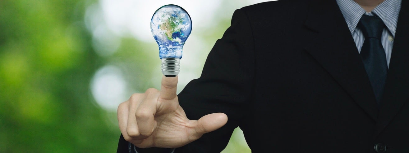 Businessman pressing earth globe in light bulb over blur green tree background,