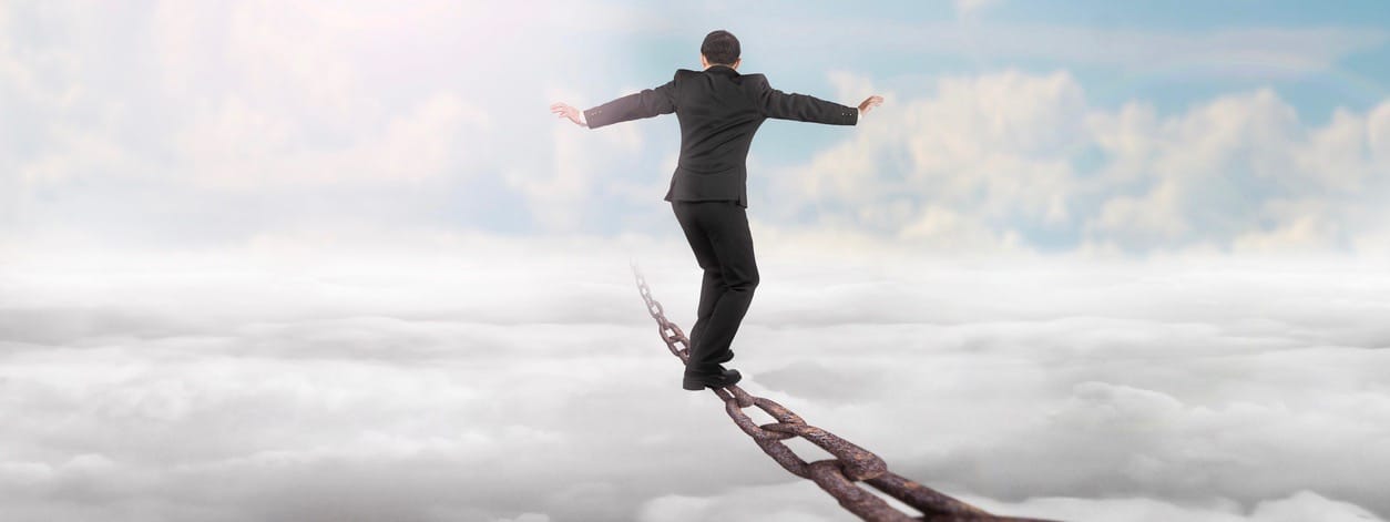 Businessman balancing on old iron chain with sky sunlight cloudscape background