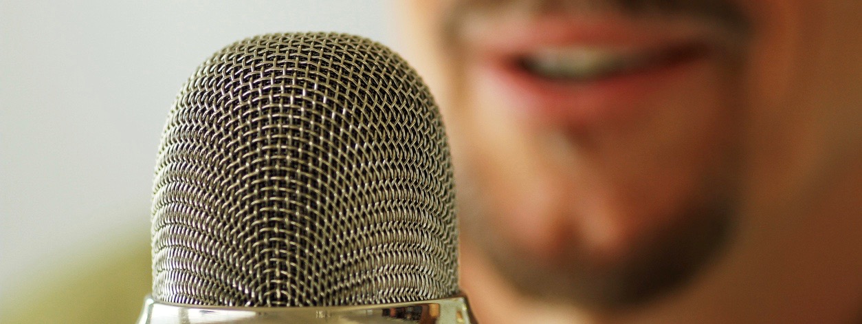 A close-up shot of a microphone with an announcer in the background recording a podcast.