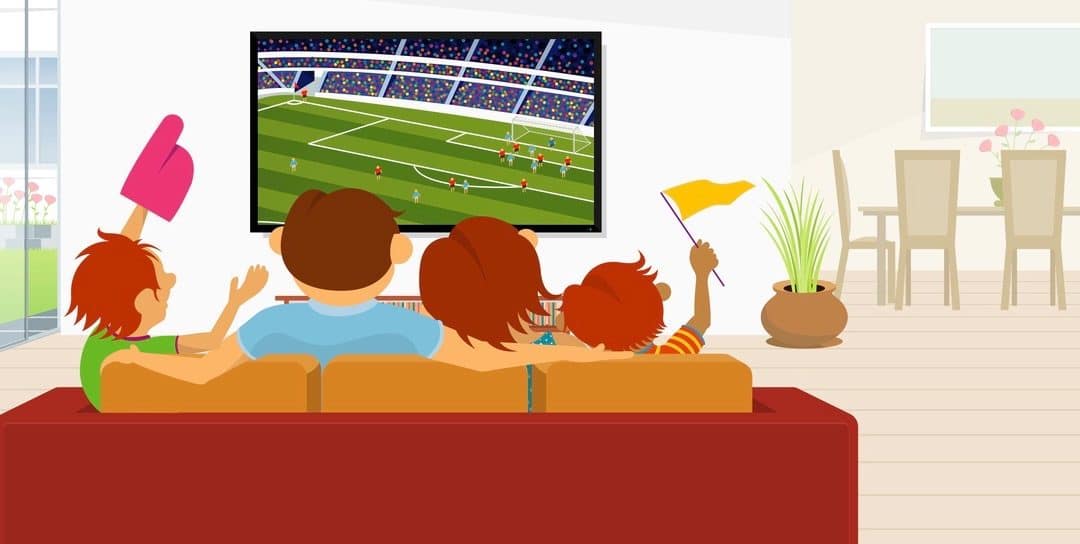Family of 4 members sitting on a red sofa in their living room inside their house watching a soccer game on a large flat television during the day