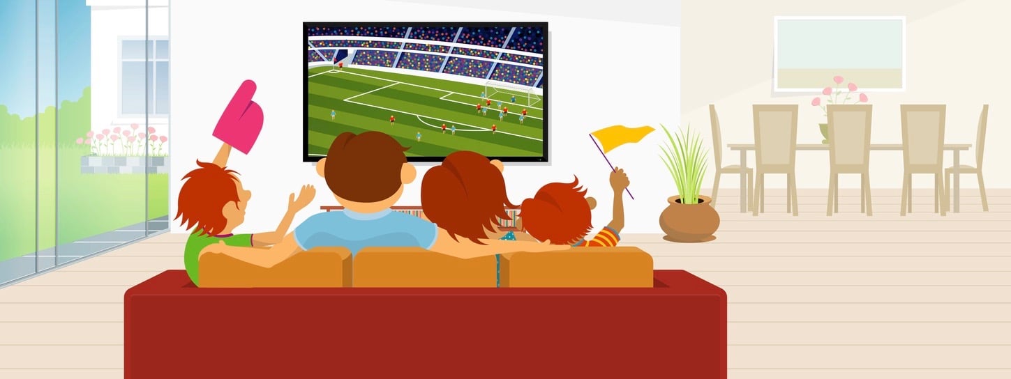 Family of 4 members sitting on a red sofa in their living room inside their house watching a soccer game on a large flat television during the day