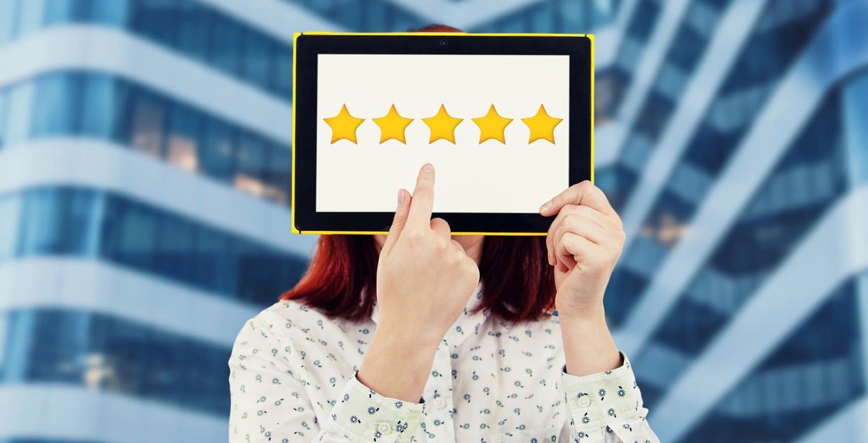 Young businesswoman covering her face using a digital tablet with five golden stars on the screen trying to choose a feedback. Excellent customer service rating concept.