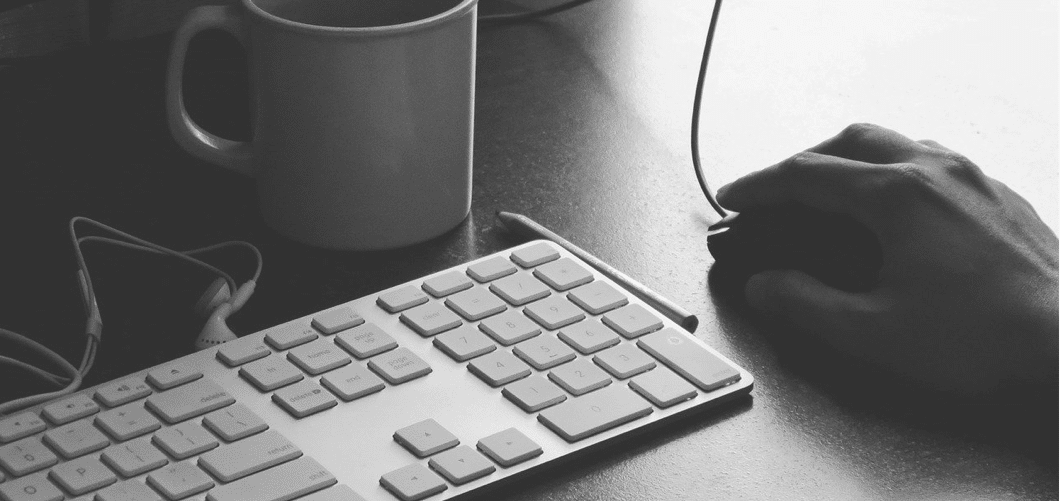 A hand on a computer mouse, a keyboard and a mug. 