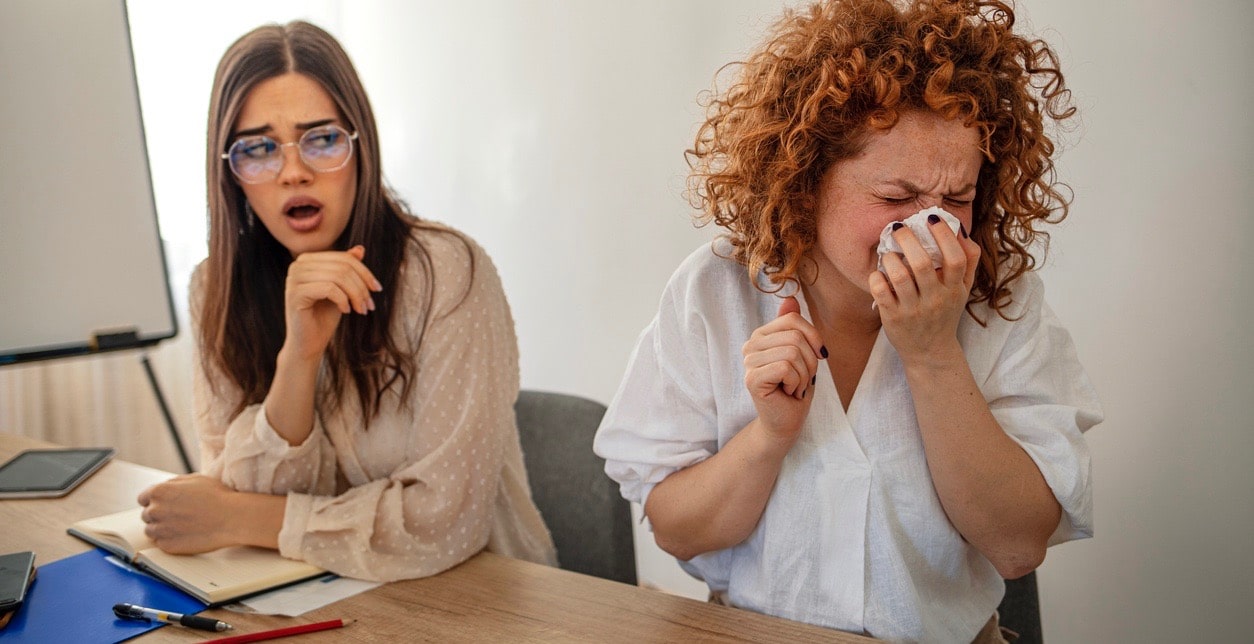 Cropped shot of a sick businessperson working with a colleague and sneezing in the office. 