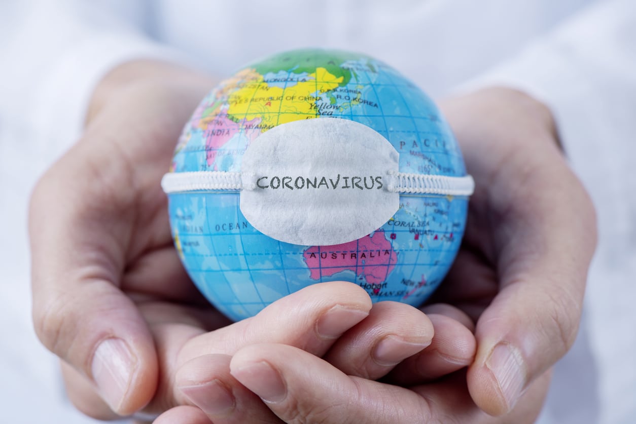 closeup of a caucasian doctor man holding a world globe with a protective mask with the word coronavirus written in it