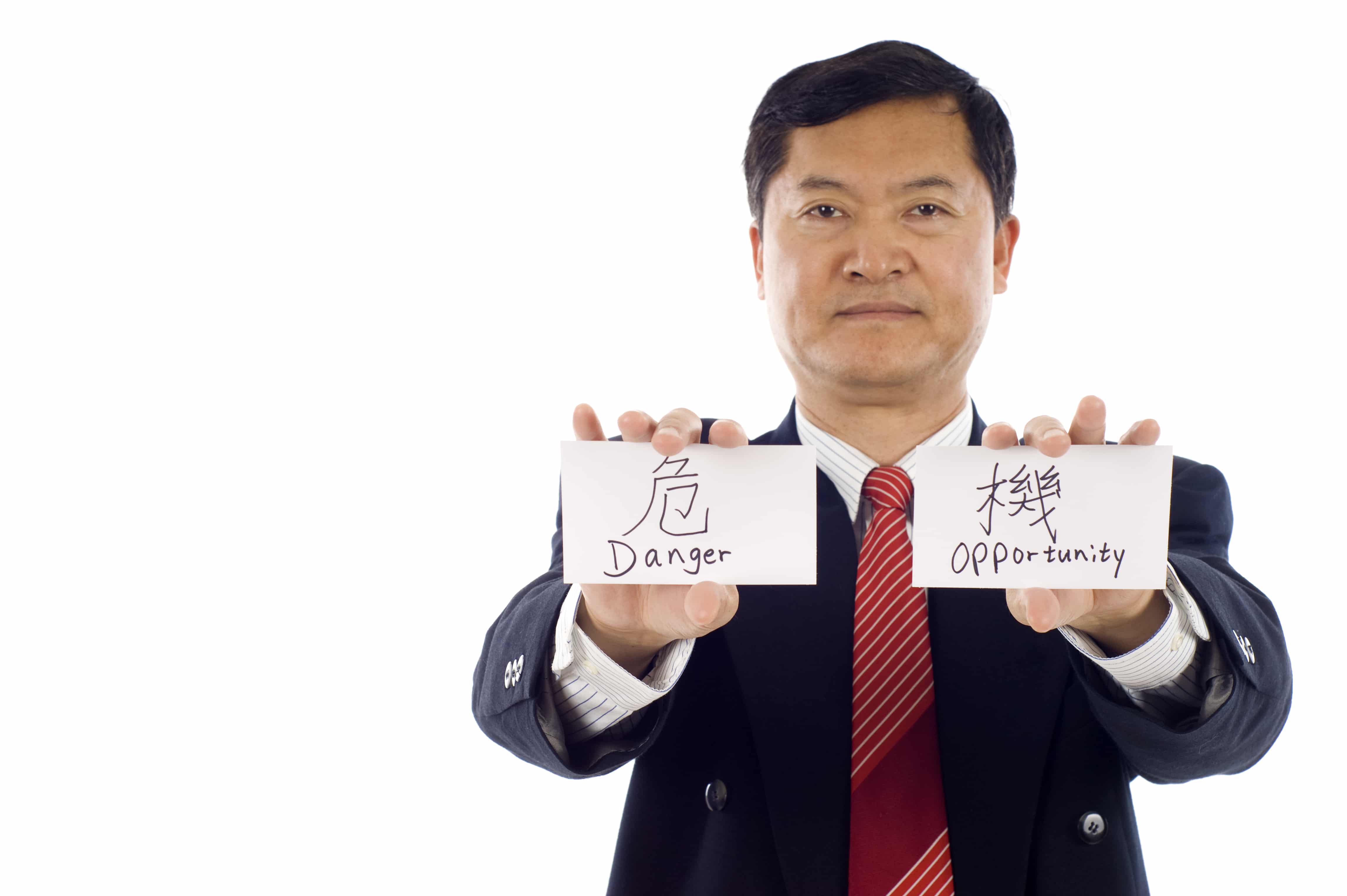 Senior Asian business man holding 2 cards, one card written the chinese word "Danger", the other "Opportunity"