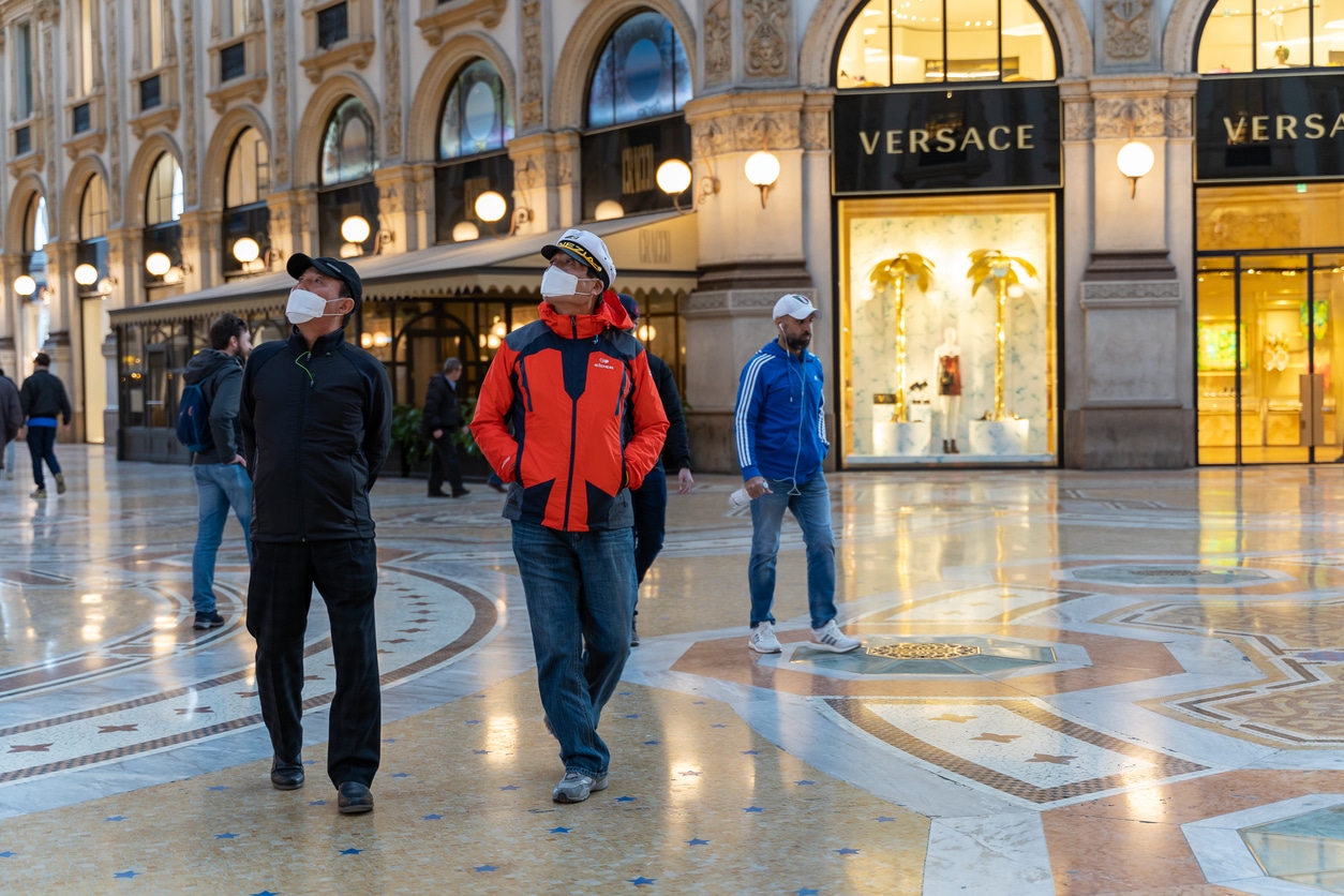 Asian men wearing white face mask walking through the Galleria Vittorio Emanuele II looking up.
