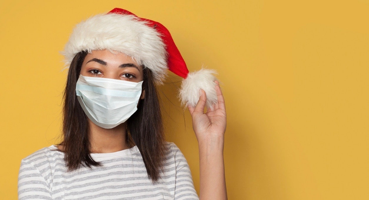 Black woman wearing a medical mask and Santa hat on yellow background