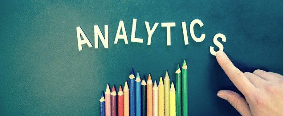 A person writing the word “analytics” out of white letters and a bunch of colored pencils below.