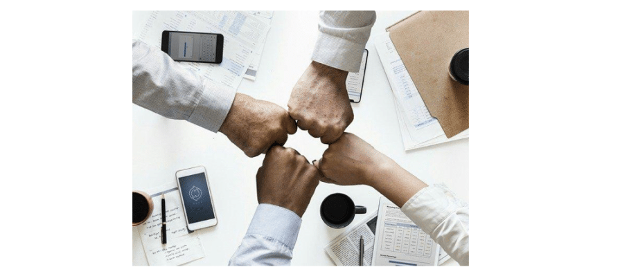 Four people fist-bumping over a desk after a successful business meeting.