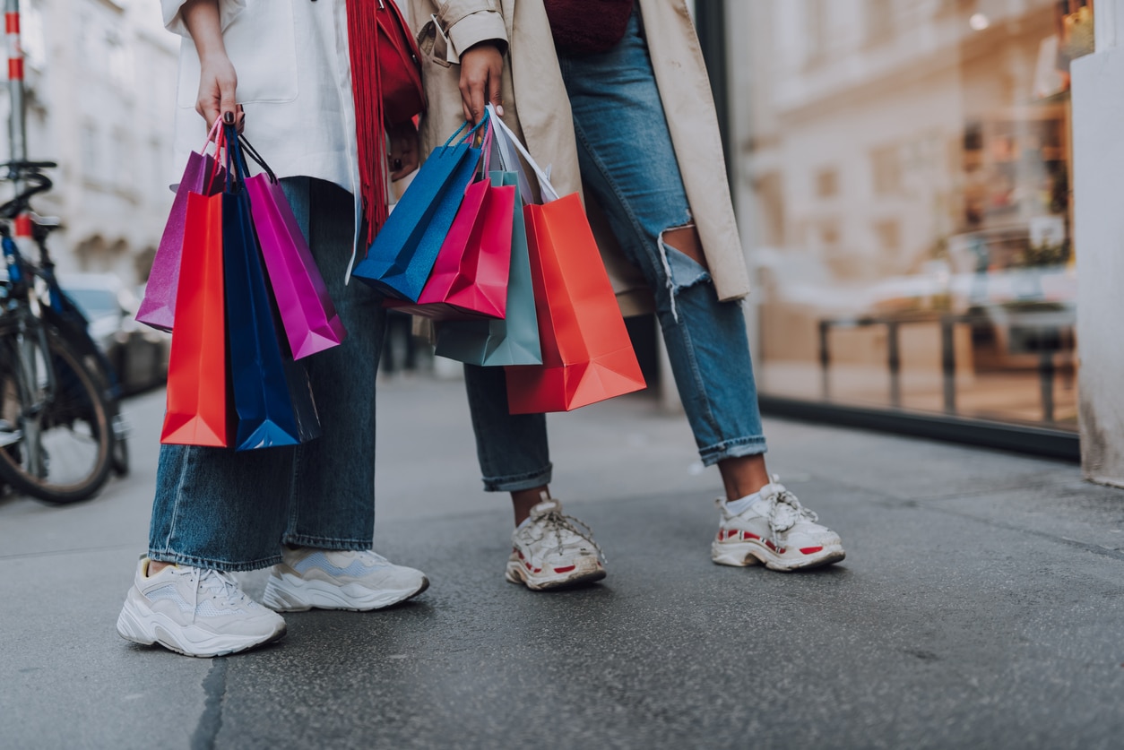 Close up of two girl in jeans and sneakers holding colorful shopping bags