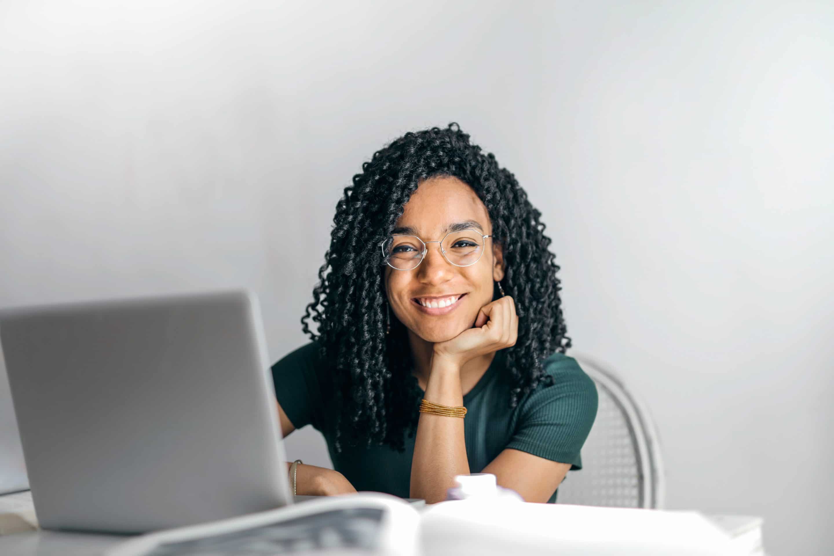 A female-presenting person of color smiling from behind a silver laptop