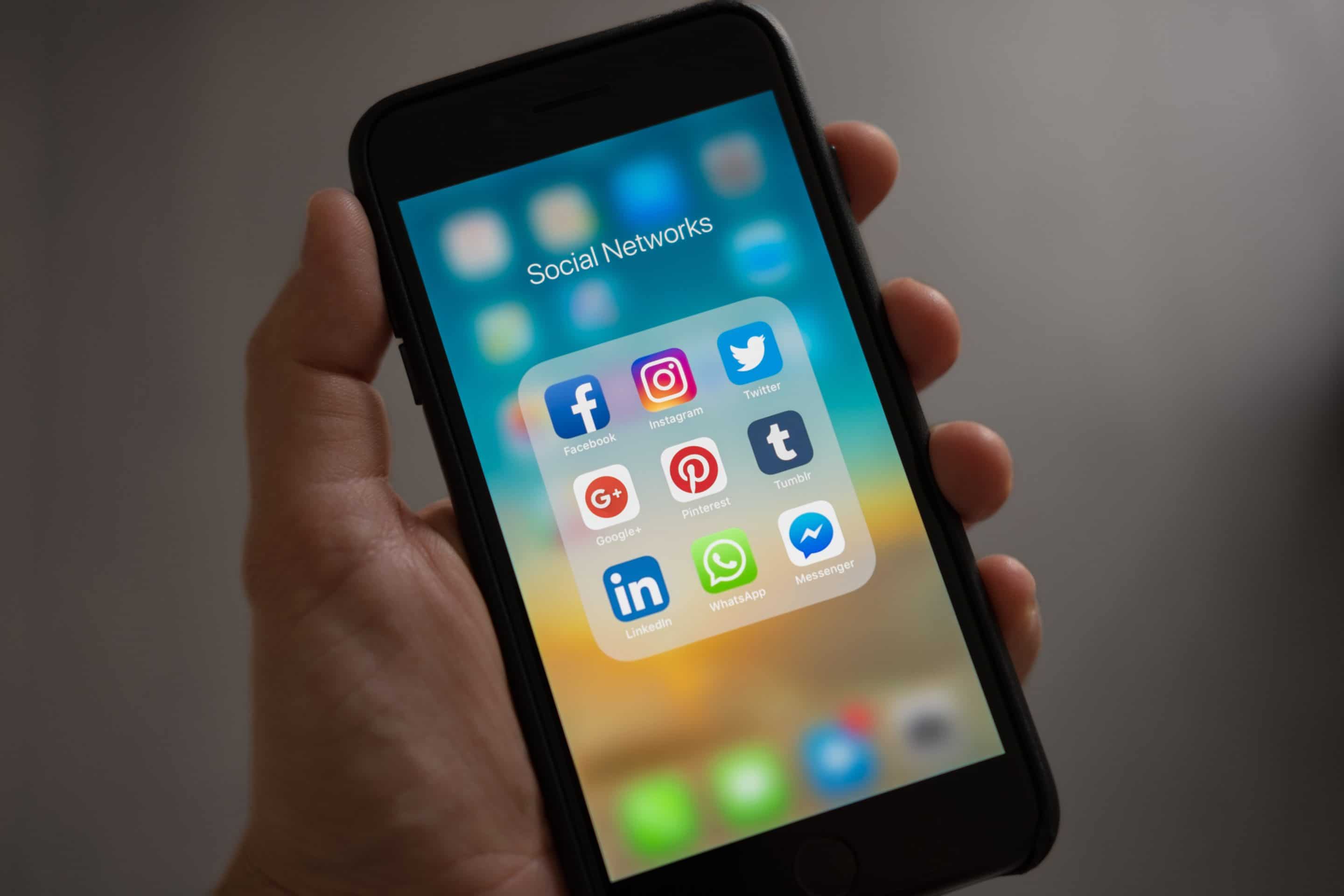 Hand holding phone with blurred background and folder of social media network icons