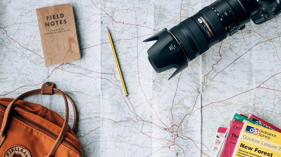 Alt-tag: A camera, bag, and other travel accessories are spread across a map.