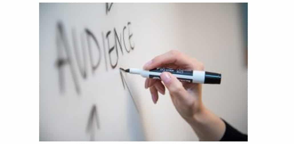 A person writing the word audience on a whiteboard