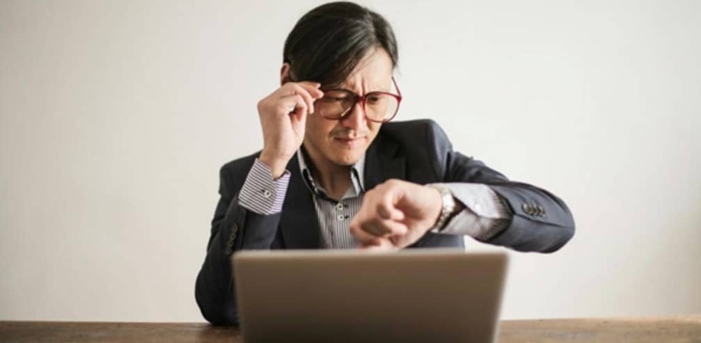 A man looking at his watch while working on his laptop