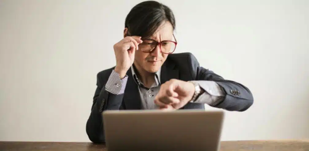 A man looking at his watch while working on his laptop 